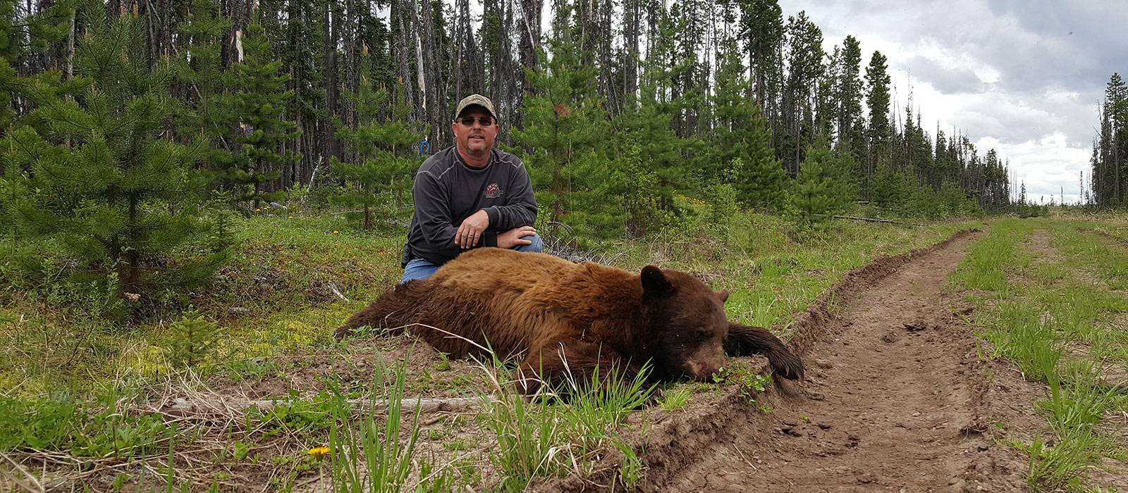 A hunter in Canada (British Columbia) sitting next to a large cinnamon colour phase black bear.